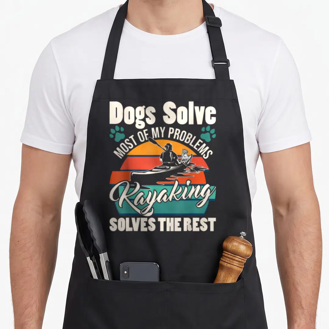 Solve dog apron - Retro graphic of person kayaking with a dog under striped sun and text reading Dogs Solve Most of My — shown on a black cotton canvas apron against a white background