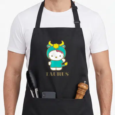 Funny zodiac taurus aprons - Hello Kitty in teal bull costume above gold TAURUS text — shown on a black cotton canvas apron against a white background
