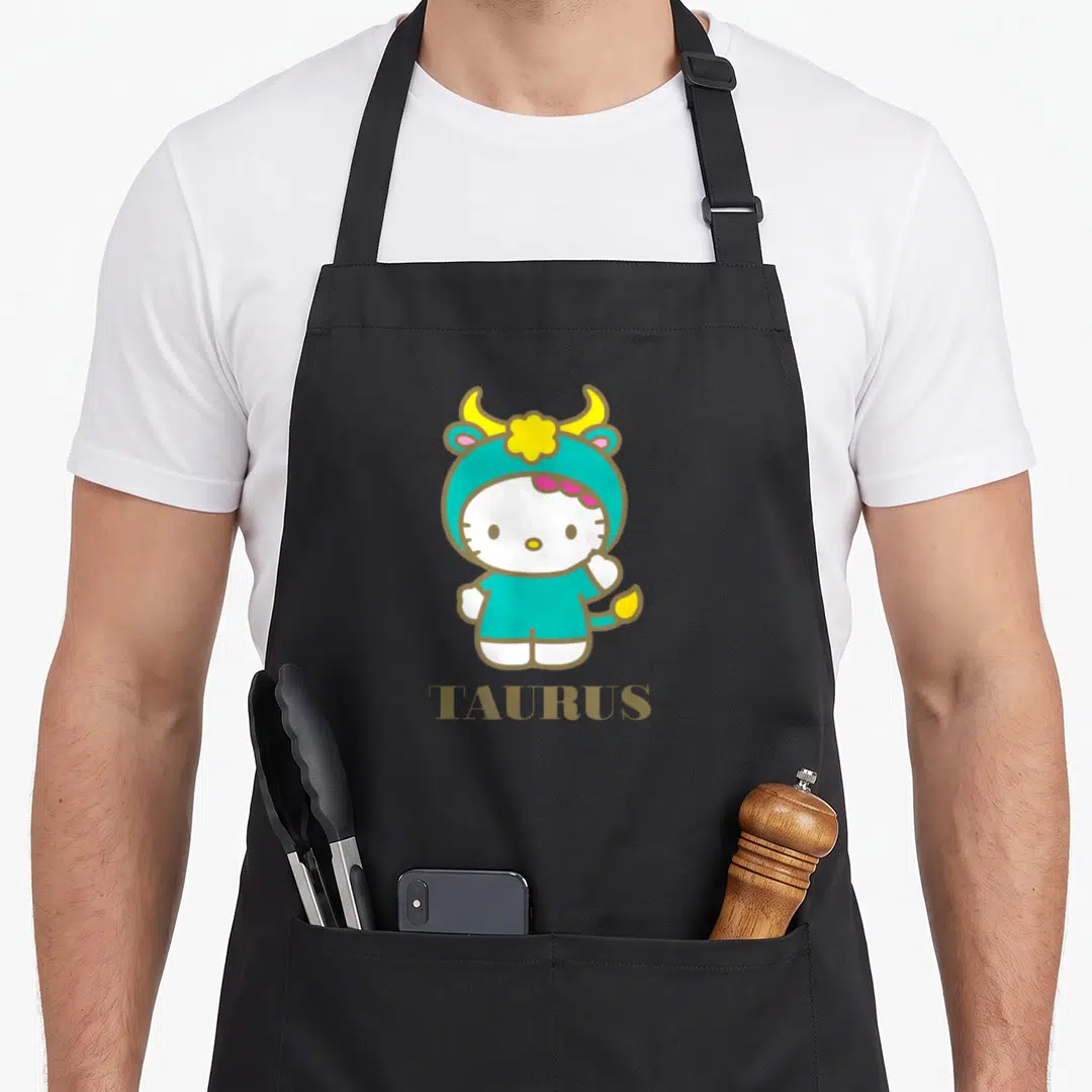 Funny zodiac taurus aprons - Hello Kitty in teal bull costume above gold TAURUS text — shown on a black cotton canvas apron against a white background