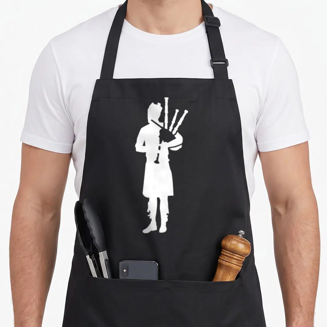 Player bagpipes apron - White silhouette of a bagpiper standing alone on a black bib apron — shown on a black cotton canvas apron against a white background