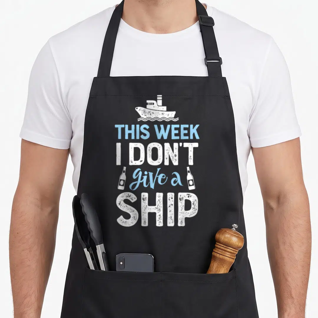 Week trips apron - White ship and two bottles flanking distressed text THIS WEEK I DON'T give a SHIP — shown on a black cotton canvas apron against a white background