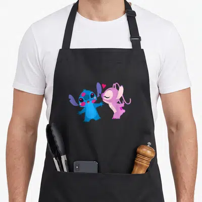 Stitch valentine angels in aprons - Blue and pink cartoon characters facing each other with a floating pink heart — shown on a black cotton canvas apron against a white background