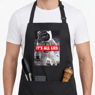 Lie conspiracy apron - Astronaut on moon with red IT'S ALL LIES banner, cartoon style, white grey black red — shown on a black cotton canvas apron against a white background