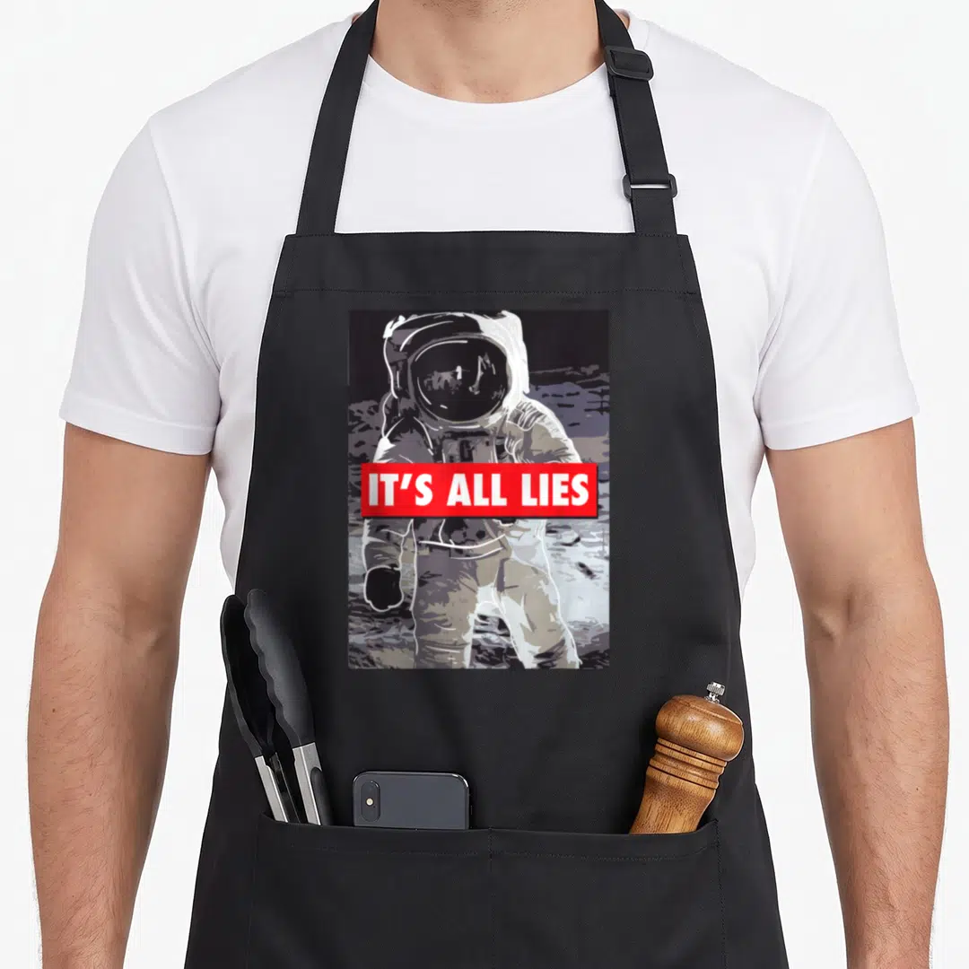 Lie conspiracy apron - Astronaut on moon with red IT'S ALL LIES banner, cartoon style, white grey black red — shown on a black cotton canvas apron against a white background