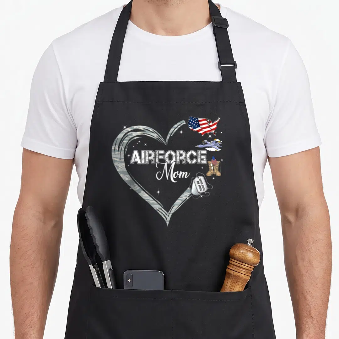 Graduation air force apron - Camo heart with AIRFORCE Mom text, jet, boots, and dog tags on grey background — shown on a black cotton canvas apron against a white background