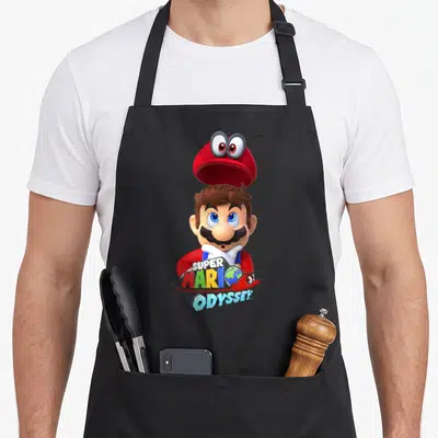 Odyssey game aprons - Mario with floating red hat and colorful Super Mario Odyssey logo text over a globe — shown on a black cotton canvas apron against a white background