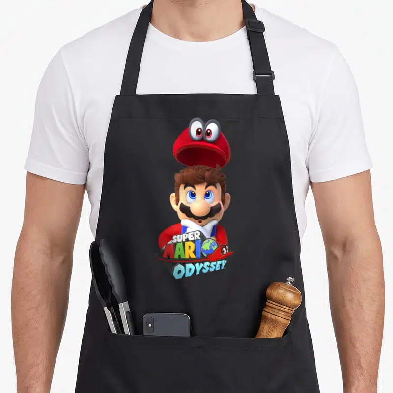 Odyssey game aprons - Mario with floating red hat and colorful Super Mario Odyssey logo text over a globe — shown on a black cotton canvas apron against a white background