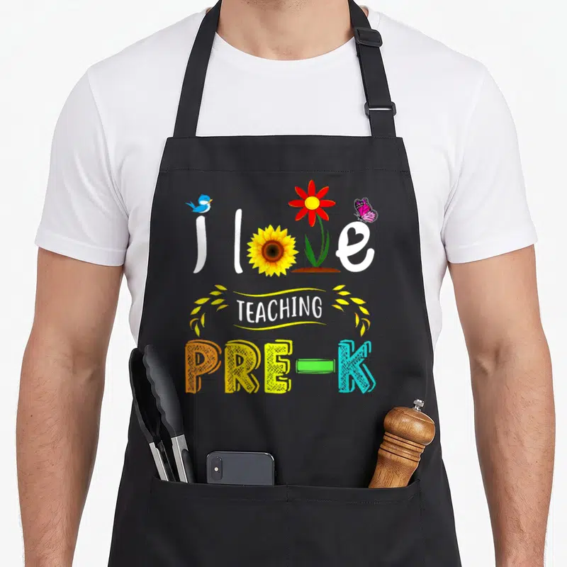 Teaching preschool teacher apron - Love text with bird sunflower red flower butterfly TEACHING PRE-K colorful letters — shown on a black cotton canvas apron against a white background