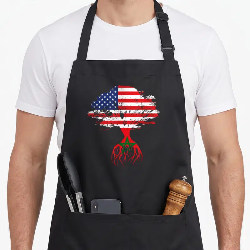 Root morocco american flag apron - Distressed tree with USA flag canopy and Morocco flag roots in red white blue — shown on a black cotton canvas apron against a white background