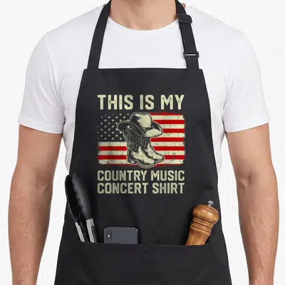 Cowboy country kitchen apron - Distressed USA flag with cowboy hat boots and text This Is My Country Music Concert Shirt — shown on a black cotton canvas apron against a white background