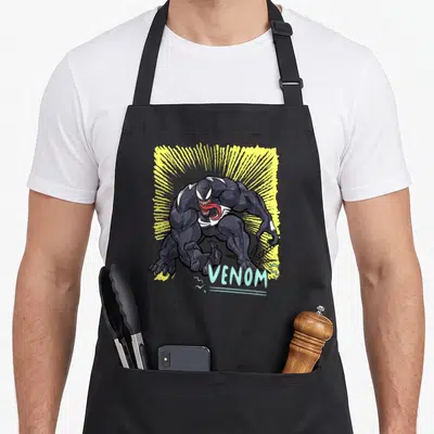 Pop marker apron - Venom character crouching before yellow sunburst with blue text label — shown on a black cotton canvas apron against a white background