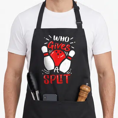 Bowler pins for aprons - Red bowling ball between two white pins with Who Gives A Split text — shown on a black cotton canvas apron against a white background