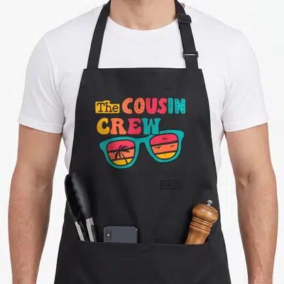 Crew making memory apron - Retro sunglasses with palm tree sunset reflection and cousin crew making memories 2023 text — shown on a black cotton canvas apron against a white background
