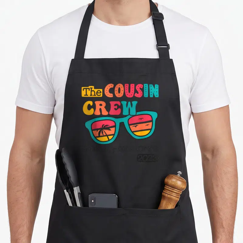 Crew making memory apron - Retro sunglasses with palm tree sunset reflection and cousin crew making memories 2023 text — shown on a black cotton canvas apron against a white background