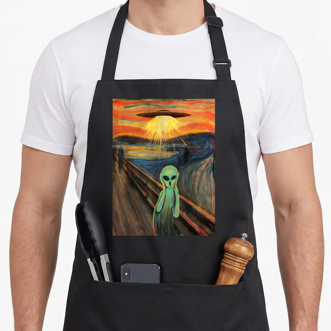 Alien painting apron - Green alien holding head on wooden bridge below UFO yellow beam — shown on a black cotton canvas apron against a white background