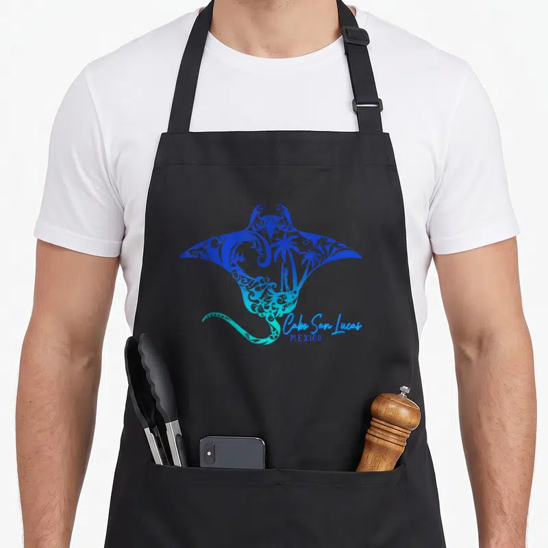 Stingray mexico apron - Blue and cyan stingray with palm tree silhouettes and Cabo San Lucas text — shown on a black cotton canvas apron against a white background