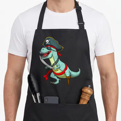 Tyrannosaurus halloween apron - Light blue cartoon dinosaur dressed as a pirate with eye patch, cutlass, and peg leg — shown on a black cotton canvas apron against a white background
