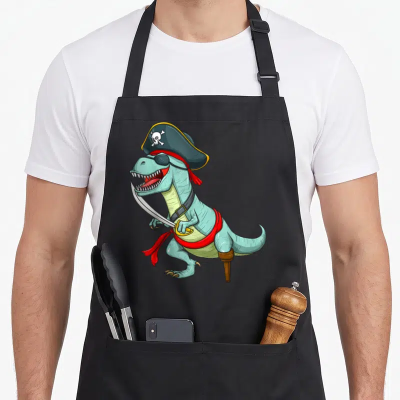 Tyrannosaurus halloween apron - Light blue cartoon dinosaur dressed as a pirate with eye patch, cutlass, and peg leg — shown on a black cotton canvas apron against a white background