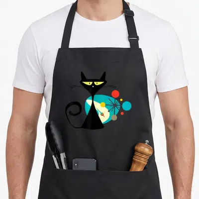 Midcentury modern apron - Black cat with yellow eyes in front of blue circle and colorful atomic sculpture — shown on a black cotton canvas apron against a white background