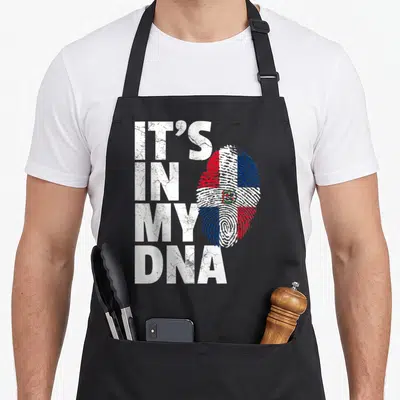 Dna pride apron - IT'S IN MY DNA text next to fingerprint filled with Dominican Republic flag colors — shown on a black cotton canvas apron against a white background