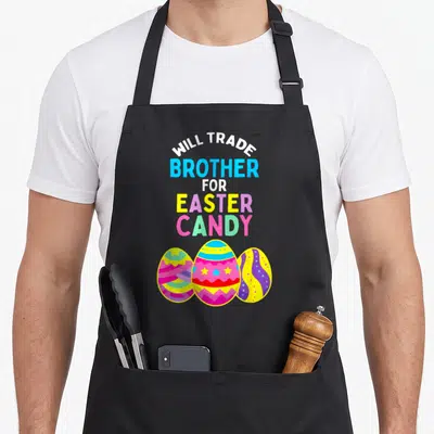 Trade easter egg apron - Stacked Will Trade Brother for Easter Candy text above three colorful cartoon Easter eggs — shown on a black cotton canvas apron against a white background