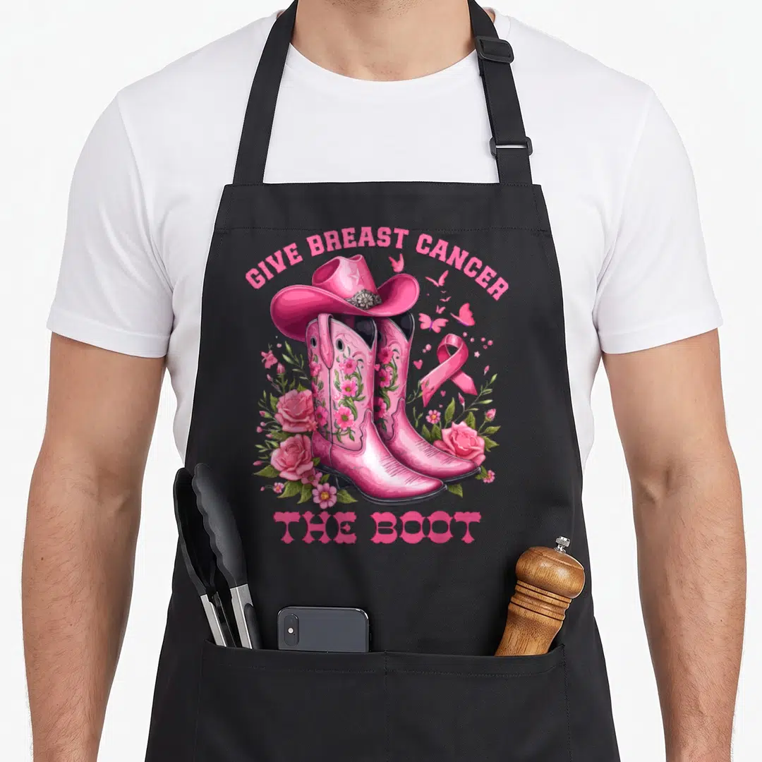 Give breast cancer awareness aprons - Pink cowboy boots with hat, ribbon, roses, and give breast cancer the boot text — shown on a black cotton canvas apron against a white background