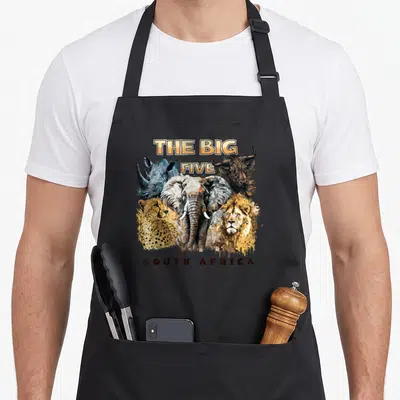 Five south african apron - The Big Five South Africa text above clustered realistic animal heads in grey, yellow — shown on a black cotton canvas apron against a white background