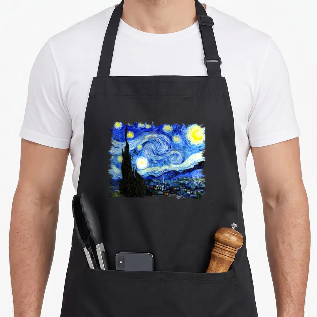 Special van gogh apron - Swirling blue night sky with yellow moon and stars above dark cypress tree and village — shown on a black cotton canvas apron against a white background