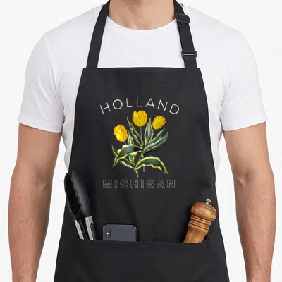 Botanical tulip apron - Yellow variegated tulips with HOLLAND MICHIGAN text in white outline — shown on a black cotton canvas apron against a white background