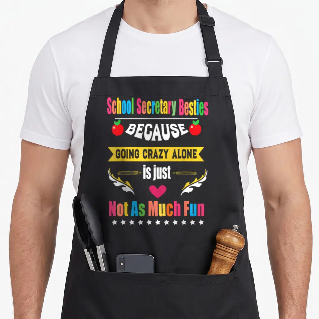 School friends apron - Colorful stacked text reading School Secretary Besties with apples, pencils, heart, and stars — shown on a black cotton canvas apron against a white background