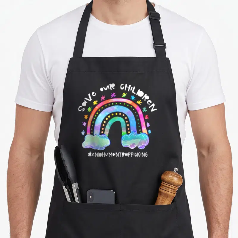 Cute save human trafficking awareness apron - Watercolor rainbow with two clouds, multicolored stars, and SAVE OUR — shown on a black cotton canvas apron against a white background