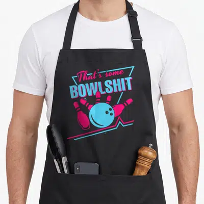 Bowlshit split apron - That's some BOWLSHIT text above blue ball and five pink pins with two zig-zag lines — shown on a black cotton canvas apron against a white background