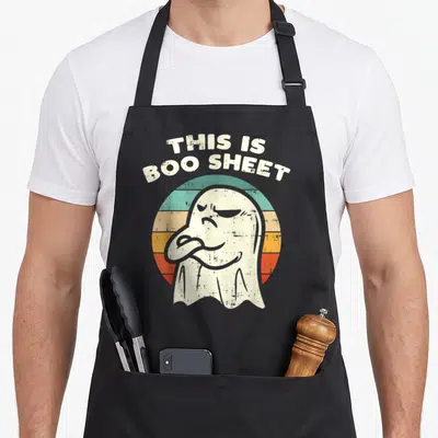 Boo halloween apron - Grumpy cartoon ghost in front of teal orange and red striped circle with arched text — shown on a black cotton canvas apron against a white background