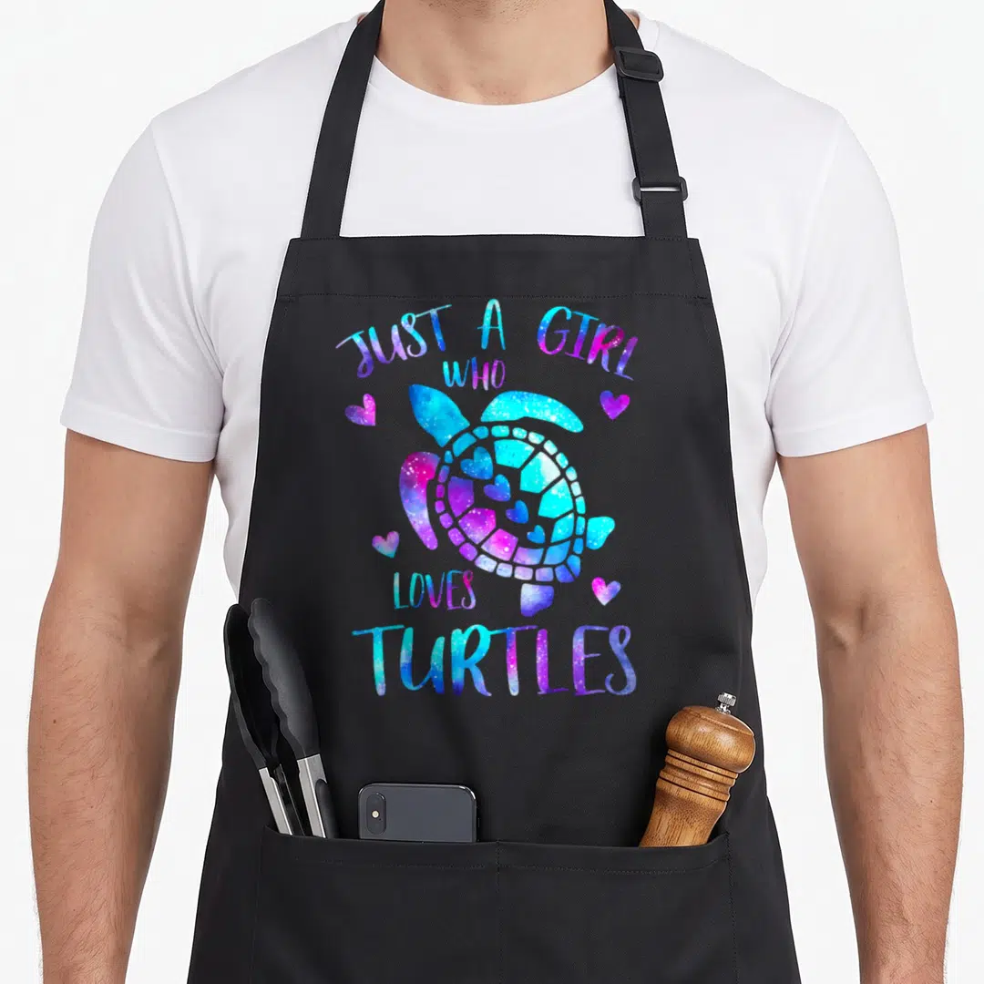 Turtle galaxies apron - Cartoon turtle with blue purple pink galaxy texture and hearts, text Just A Girl Who Loves — shown on a black cotton canvas apron against a white background