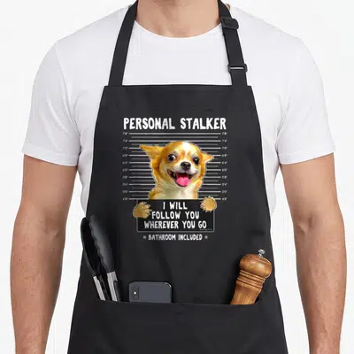 Follow personal apron - Chihuahua mugshot holding black sign with personal stalker text and height chart measurements — shown on a black cotton canvas apron against a white background