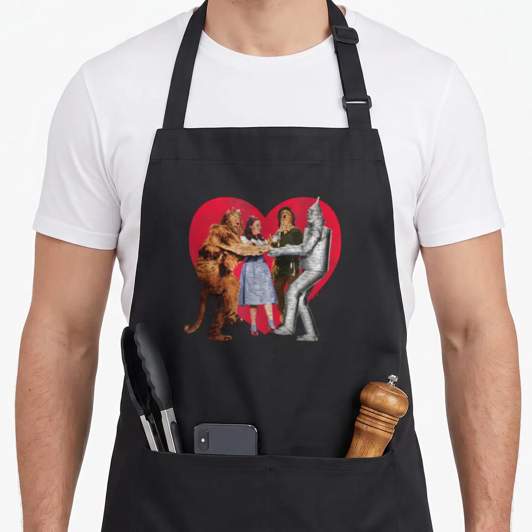 Funny wizard novelty apron - Four characters standing holding hands in front of large red heart, photo style art — shown on a black cotton canvas apron against a white background