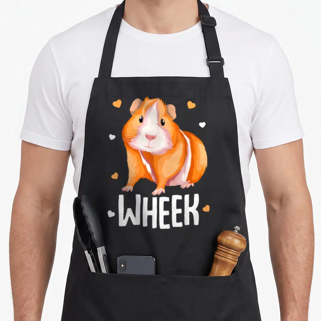 Wheek cute guinea apron - Cartoon orange and white guinea pig above WHEEK text with scattered hearts — shown on a black cotton canvas apron against a white background