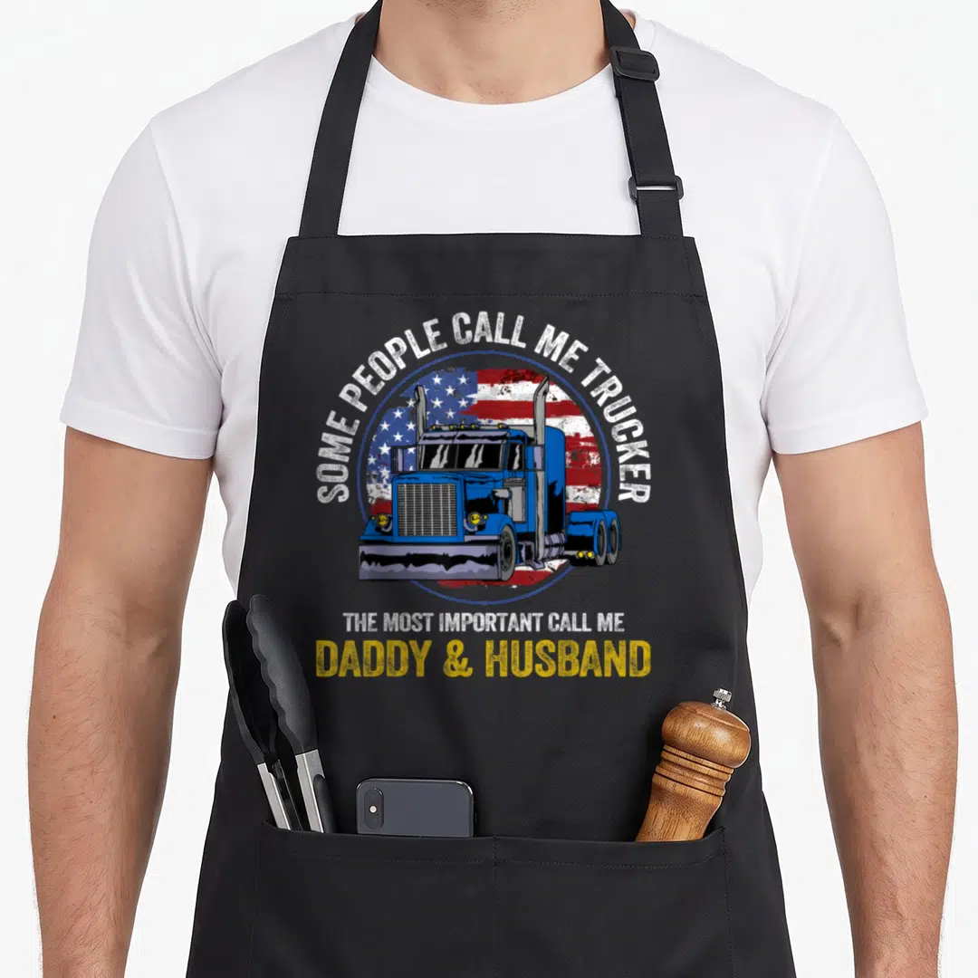 Trucker husband father day apron - Blue semi-truck over distressed USA flag with text about being a daddy and husband — shown on a black cotton canvas apron against a white background