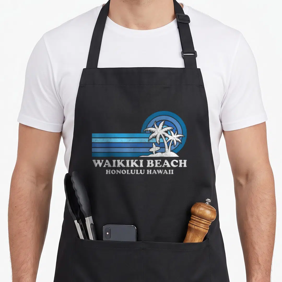 Waikiki family aprons - Retro blue and white Waikiki Beach Honolulu Hawaii graphic with two palm trees and surfer — shown on a black cotton canvas apron against a white background