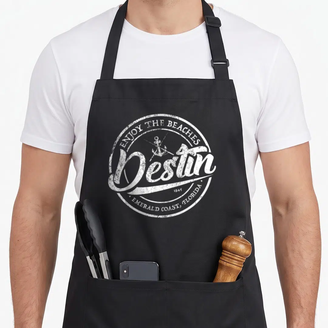 Enjoy destin apron - White distressed circular logo with anchor, Enjoy the Beaches text, and Destin script — shown on a black cotton canvas apron against a white background