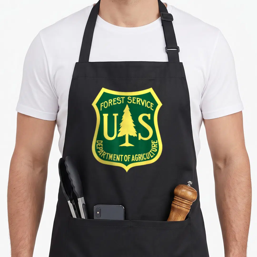 Forest service apron - Green and yellow shield with pine tree and arched text reading Forest Service Department — shown on a black cotton canvas apron against a white background