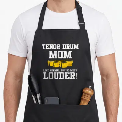 School band mom apron - TENOR DRUM MOM text above four yellow drums and louder slogan — shown on a black cotton canvas apron against a white background