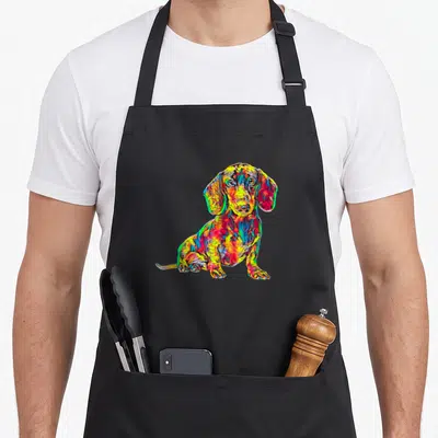 Dachshund dog breed aprons - Multicolored cartoon dachshund in red yellow blue and green sitting pose — shown on a black cotton canvas apron against a white background