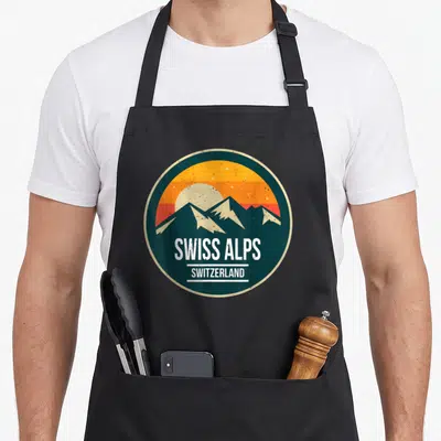 Mountain swiss apron - Retro circular badge with SWISS ALPS text and striped sunset over teal mountains — shown on a black cotton canvas apron against a white background
