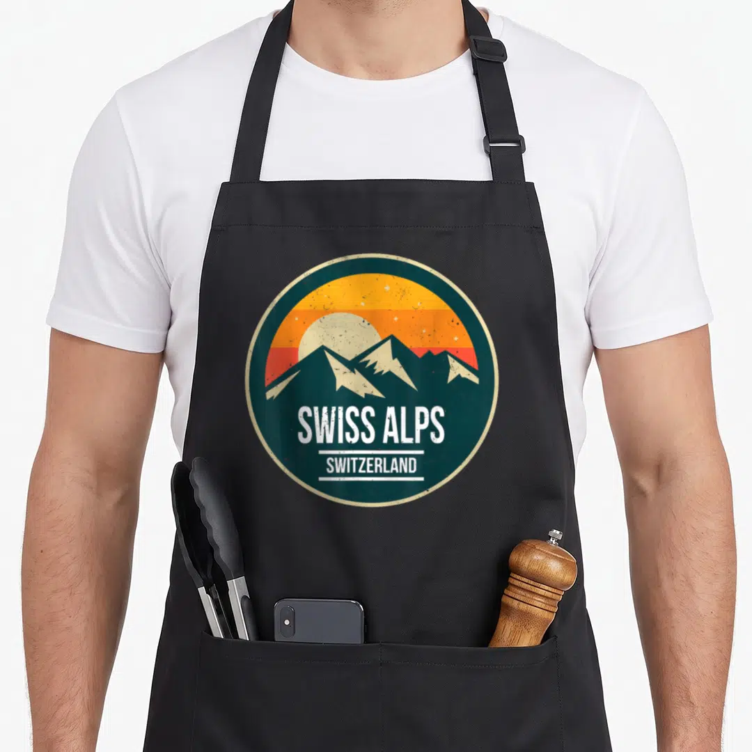 Mountain swiss apron - Retro circular badge with SWISS ALPS text and striped sunset over teal mountains — shown on a black cotton canvas apron against a white background