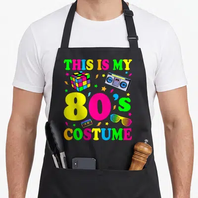 Costume 80s apron - Neon 80s text with boombox, cube, cassette, and glasses in pink yellow green blue — shown on a black cotton canvas apron against a white background