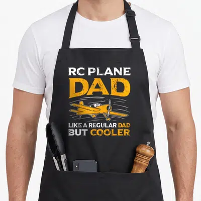 Pilot model airplane apron - Orange and white distressed text RC Plane Dad surrounding a model airplane graphic — shown on a black cotton canvas apron against a white background
