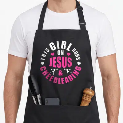 Run cheerleading apron - Circular white and pink text reading THIS GIRL RUNS ON JESUS CHEERLEADING with heart — shown on a black cotton canvas apron against a white background