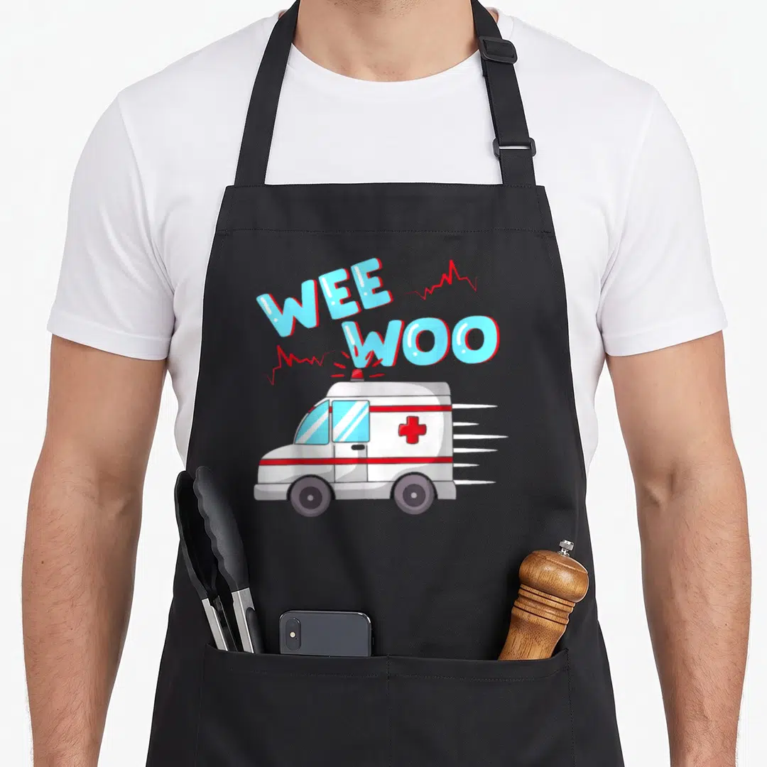 Ems ambulance apron - Stacked Wee Woo text over cartoon ambulance with red heartbeat lines and blue windows — shown on a black cotton canvas apron against a white background
