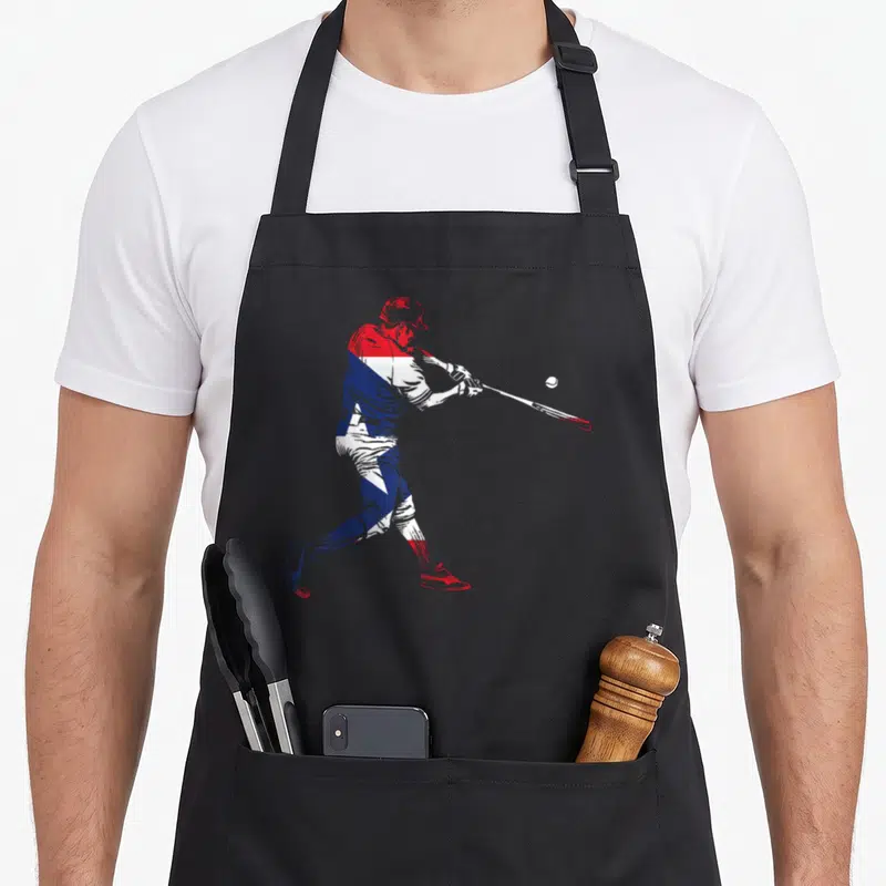 Puerto kitchen island apron - Baseball player swinging bat in red white and blue silhouette — shown on a black cotton canvas apron against a white background